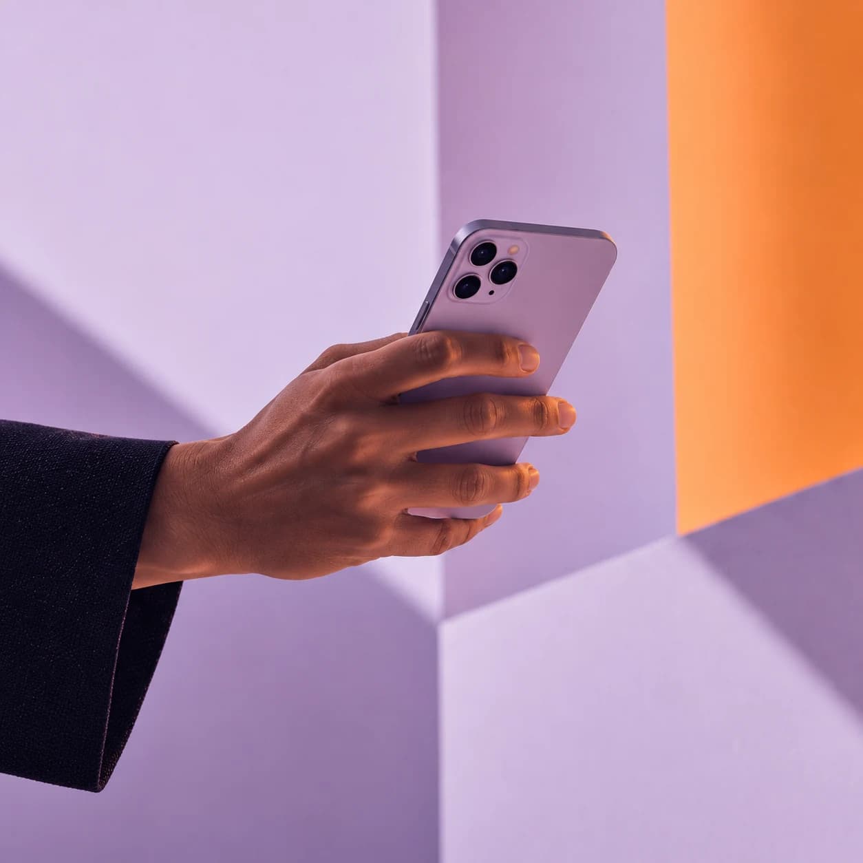 A hand holding a lilac phone against lilac and orange walls.